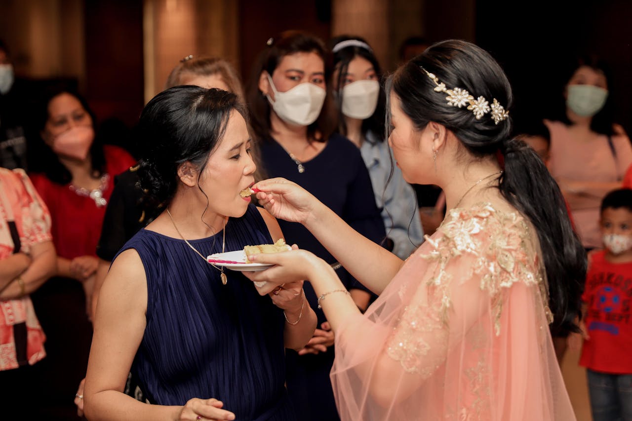 ours-journey A woman feeds cake to another at a lively family gathering with guests.